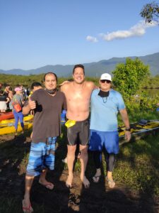 Três homens abraçados, um deles sem camisa, posam para a câmera